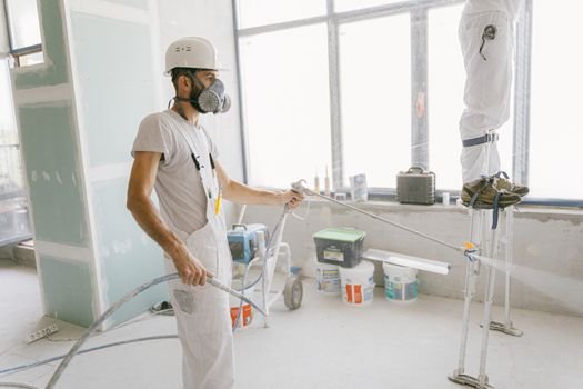 Two construction workers wearing protective gear and painting interior walls for a renovation project.